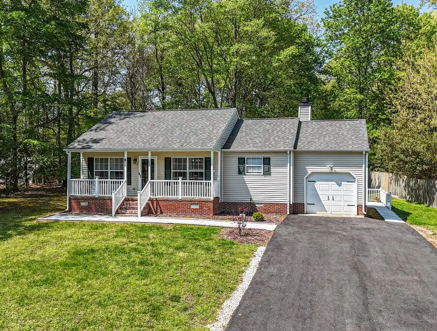 Cozy single-story house with a garage and front porch in a green wooded area.