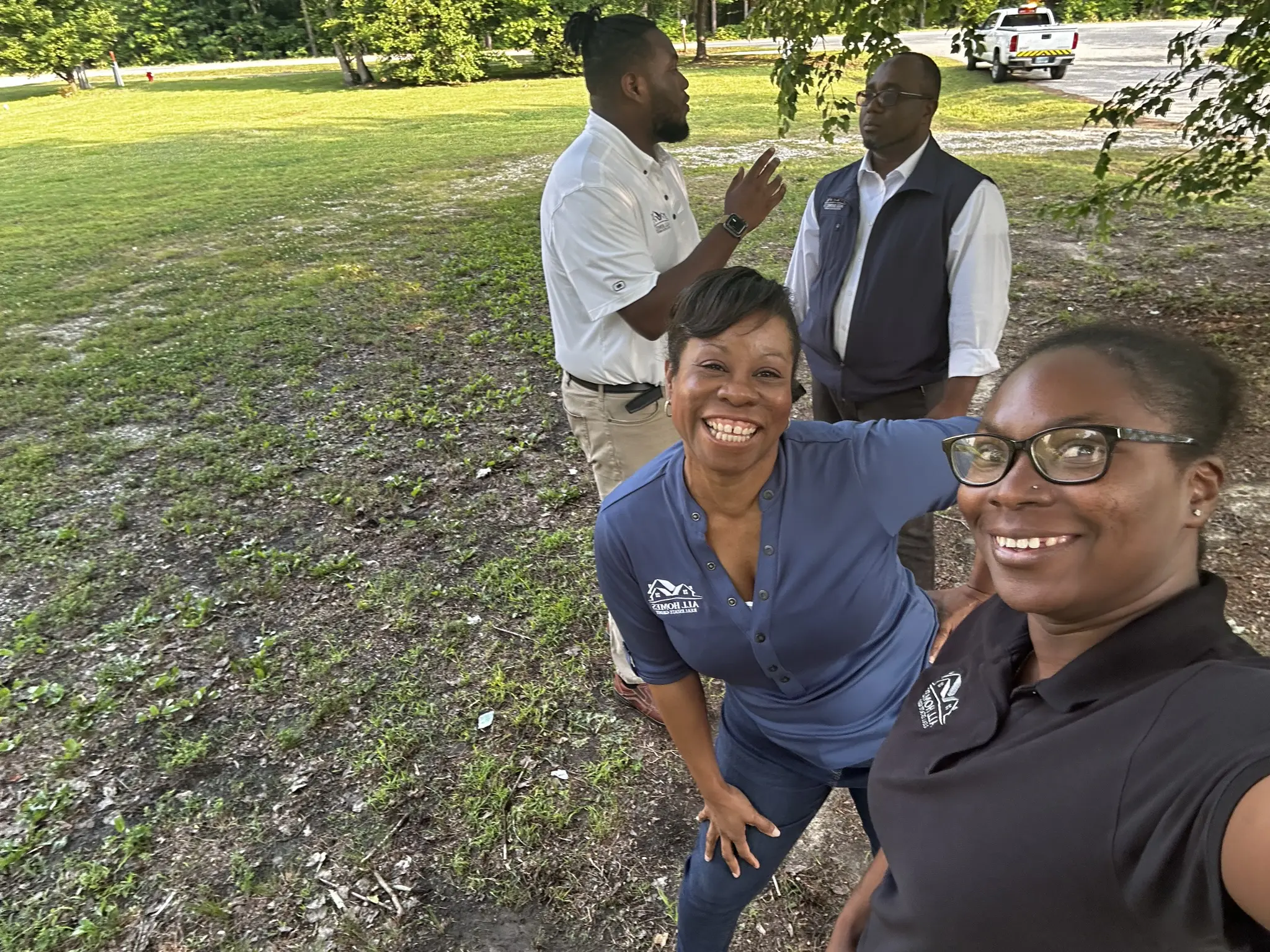 Three people smiling outdoors, two posing and one talking.