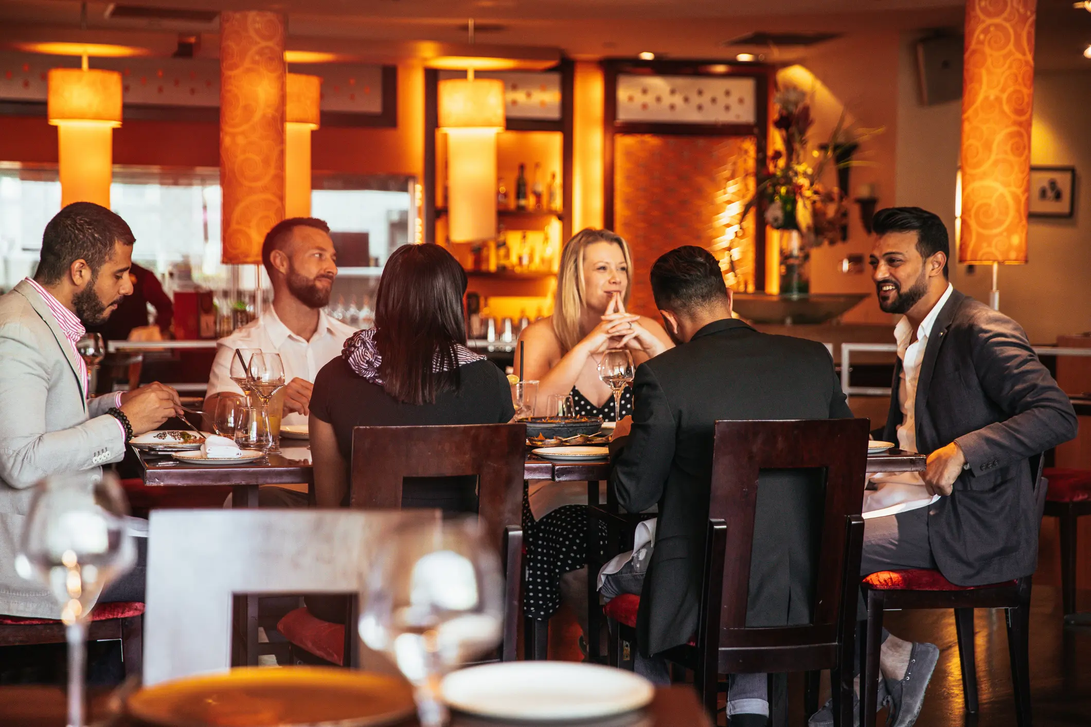 Friends enjoying a lively dinner at a warmly lit restaurant.