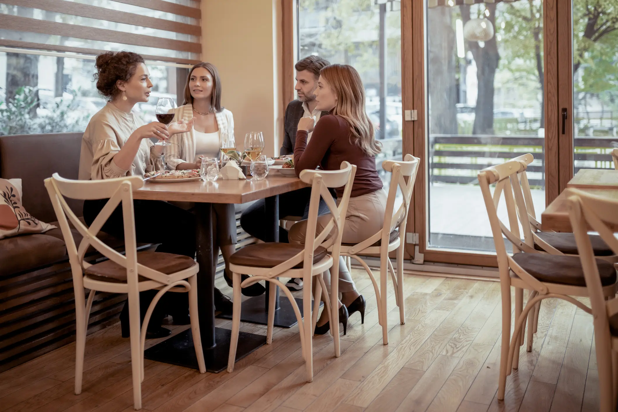 Four women wearing masks sit around a table in a café, chatting and drinking coffee.
