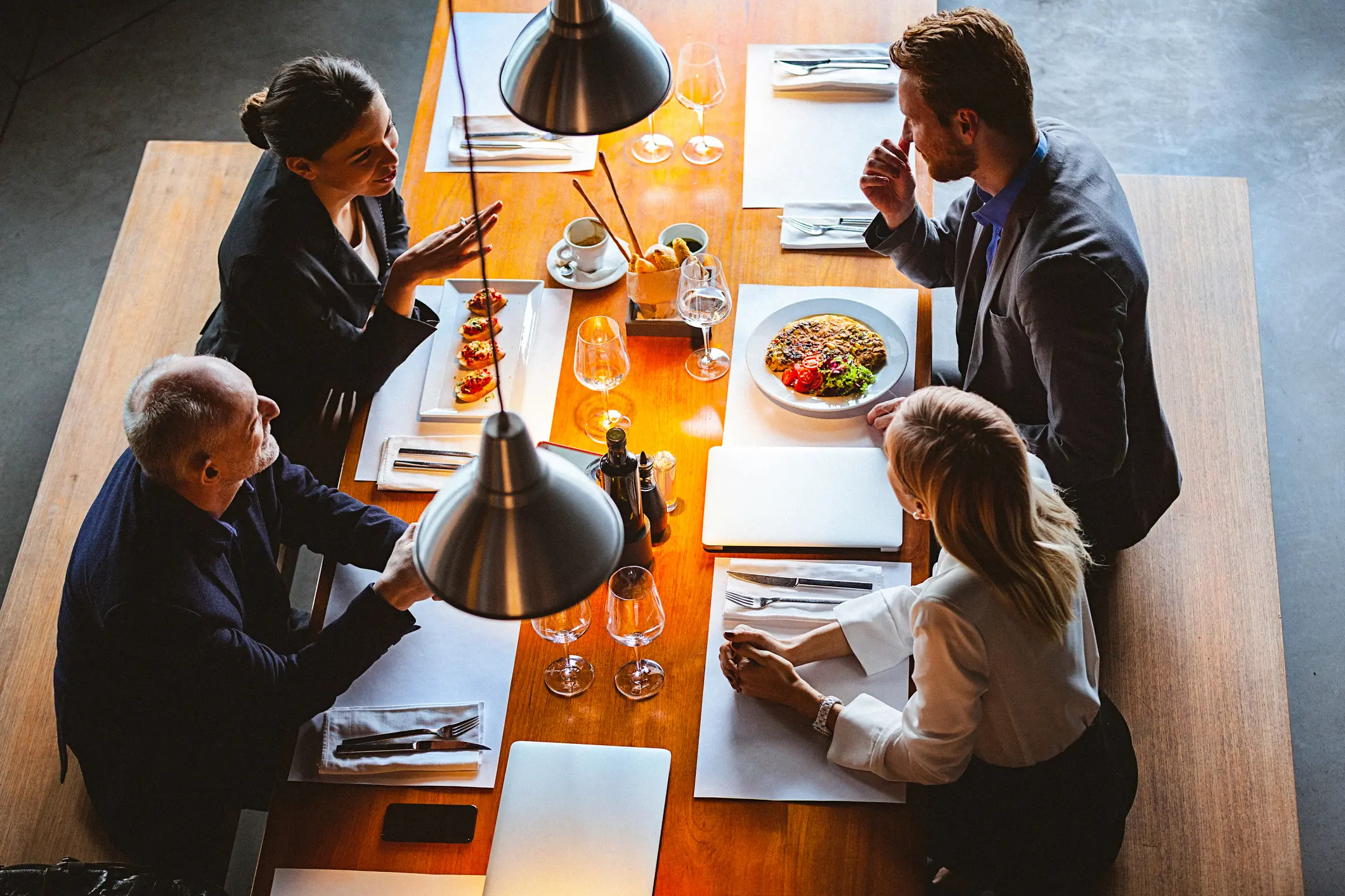 Four professionals discussing work over lunch at a wooden table.