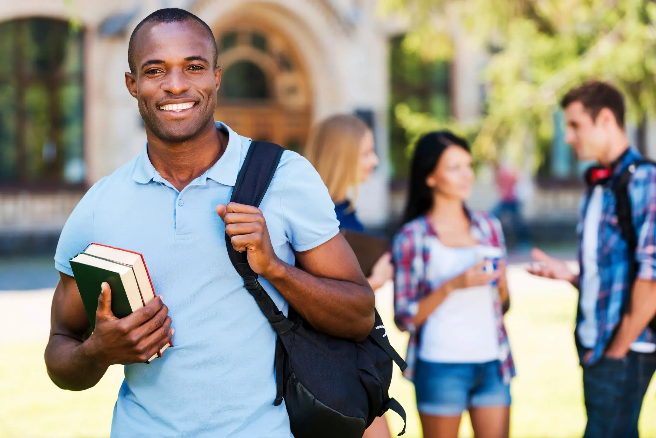 Smiling male student holding books and backpack outdoors.