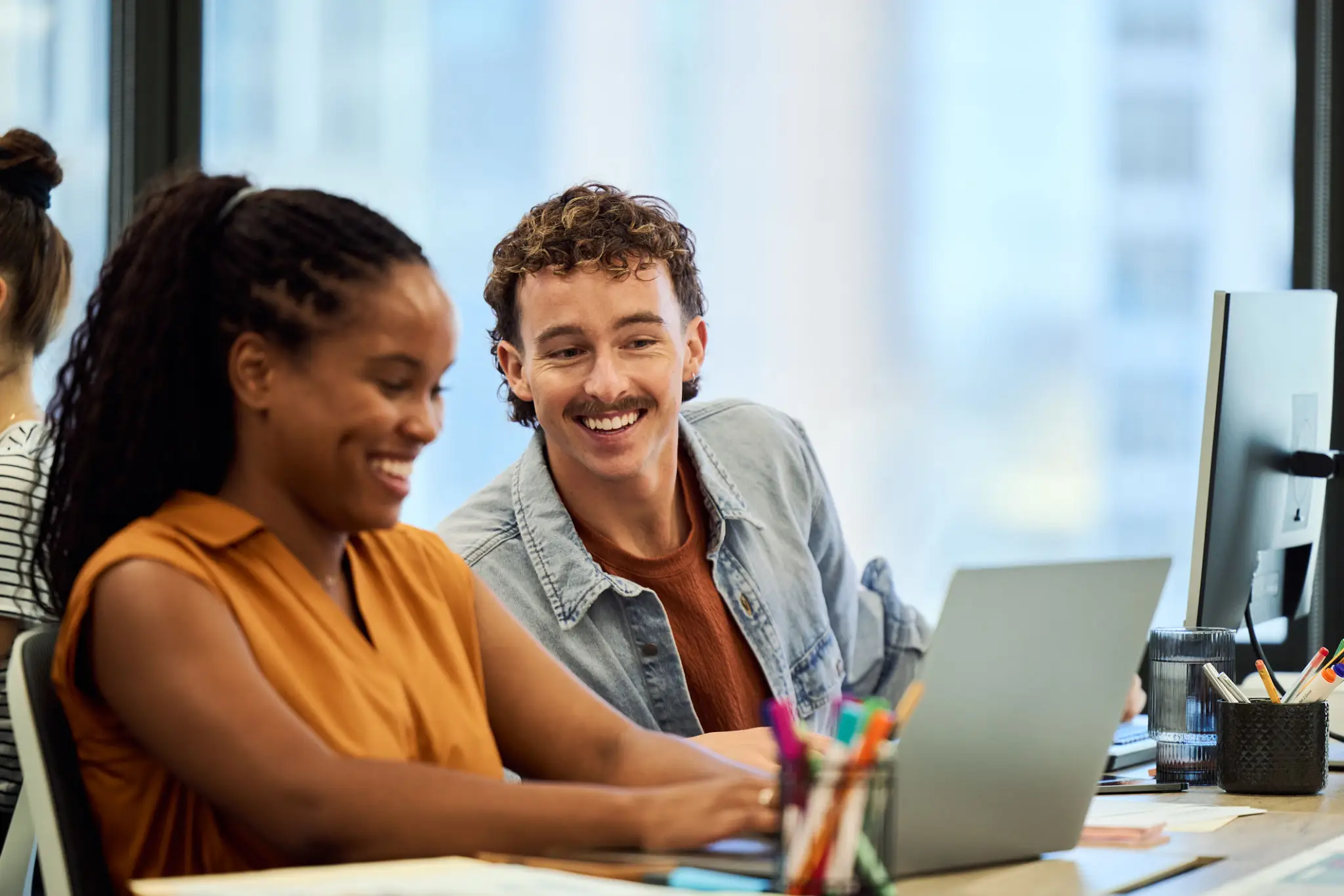 Two colleagues smiling and working together on a laptop.
