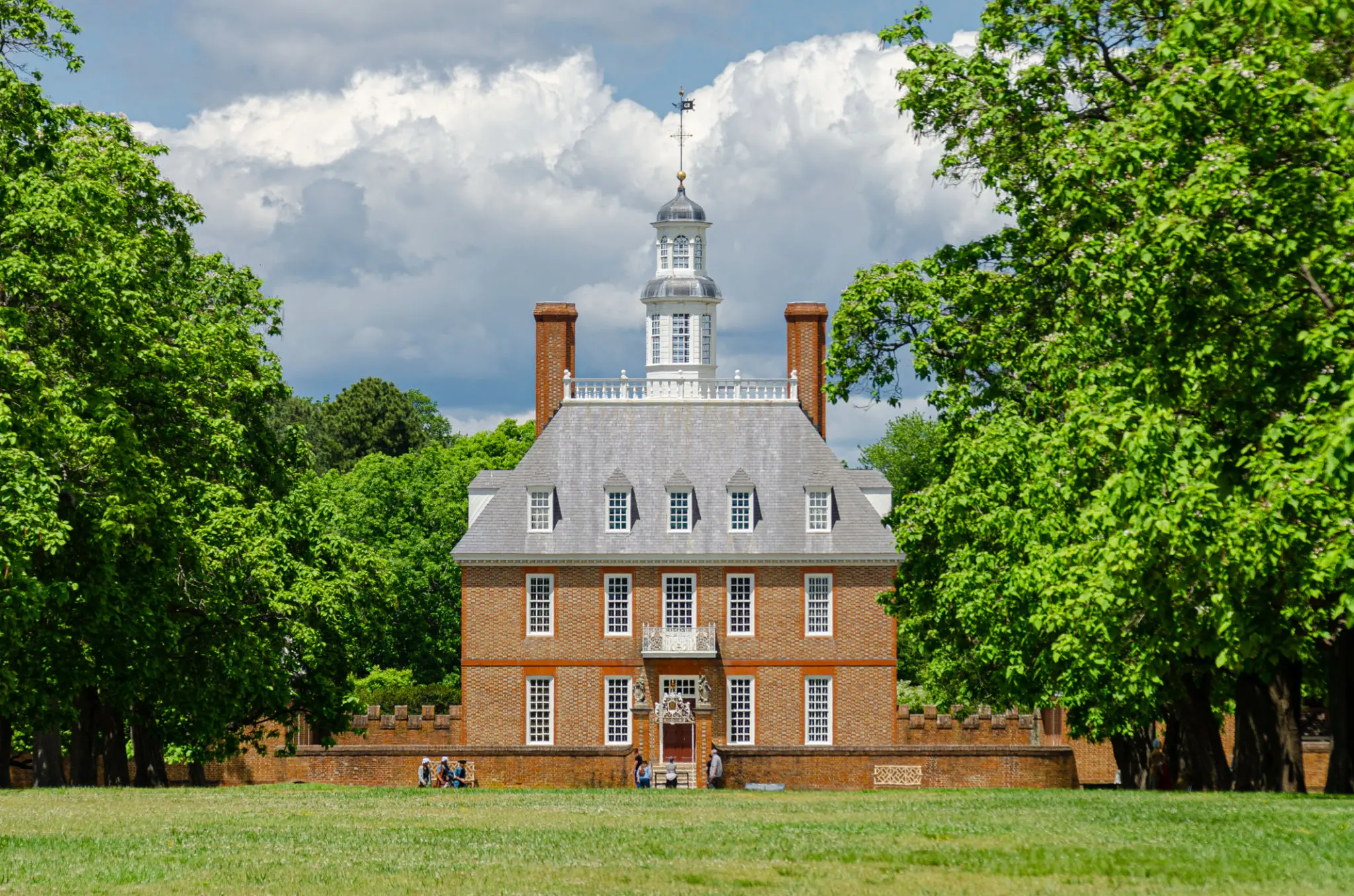 Historic brick mansion with a tall white cupola amid green trees.