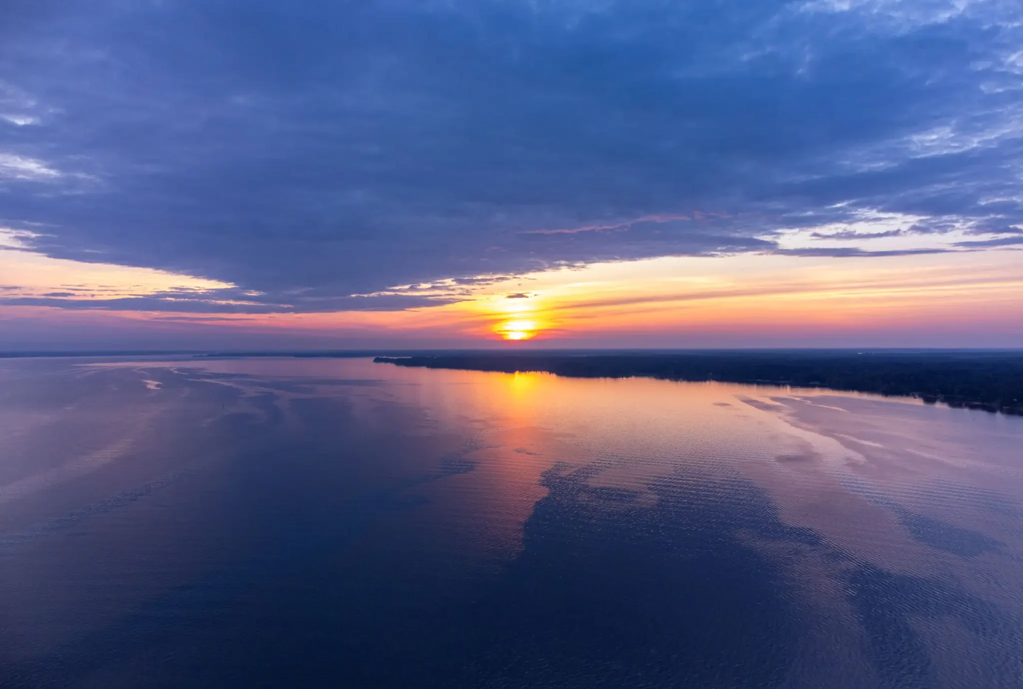 Sunset reflecting on calm water with a dramatic sky.