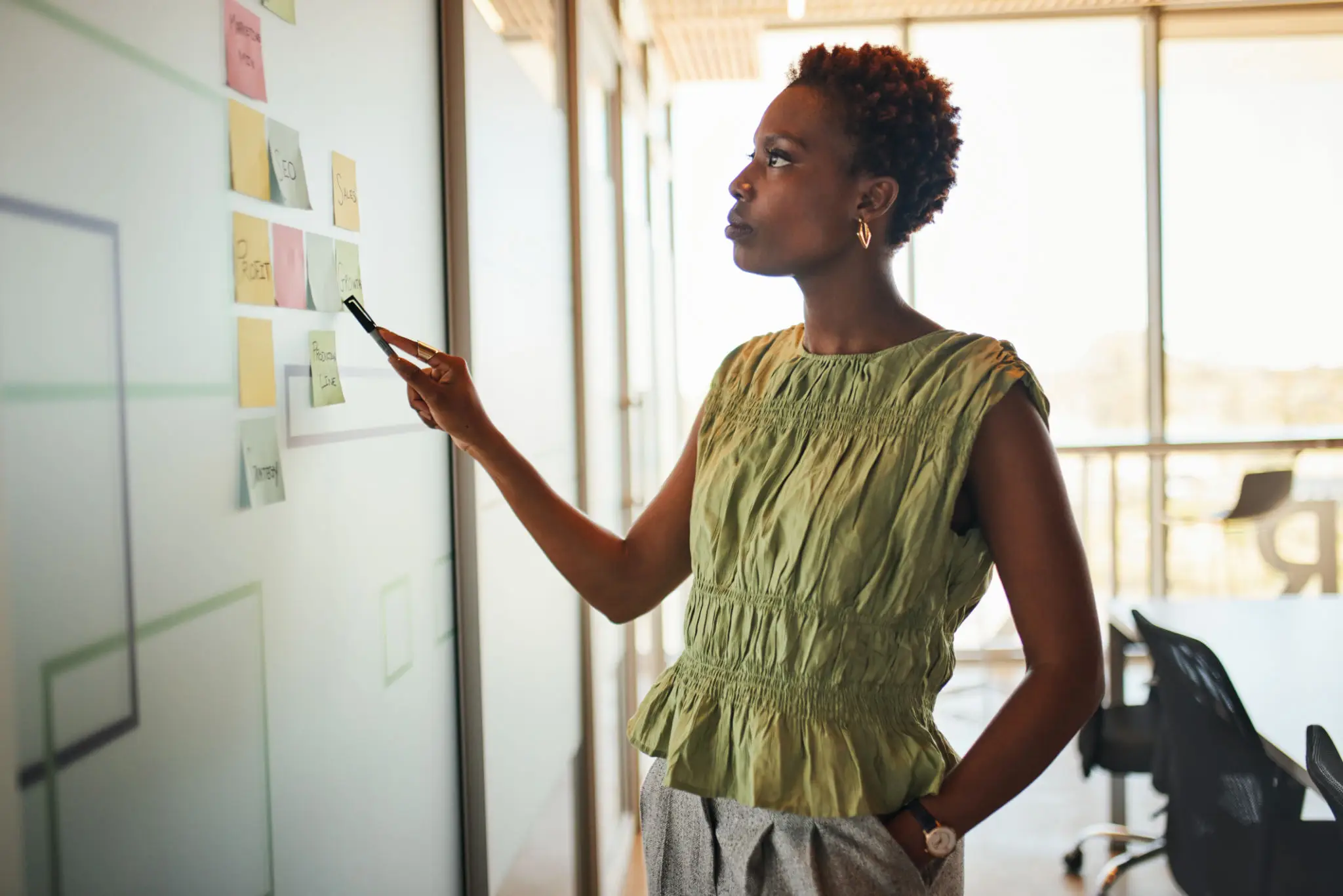 A woman in a green top pointing at sticky notes on a wall.