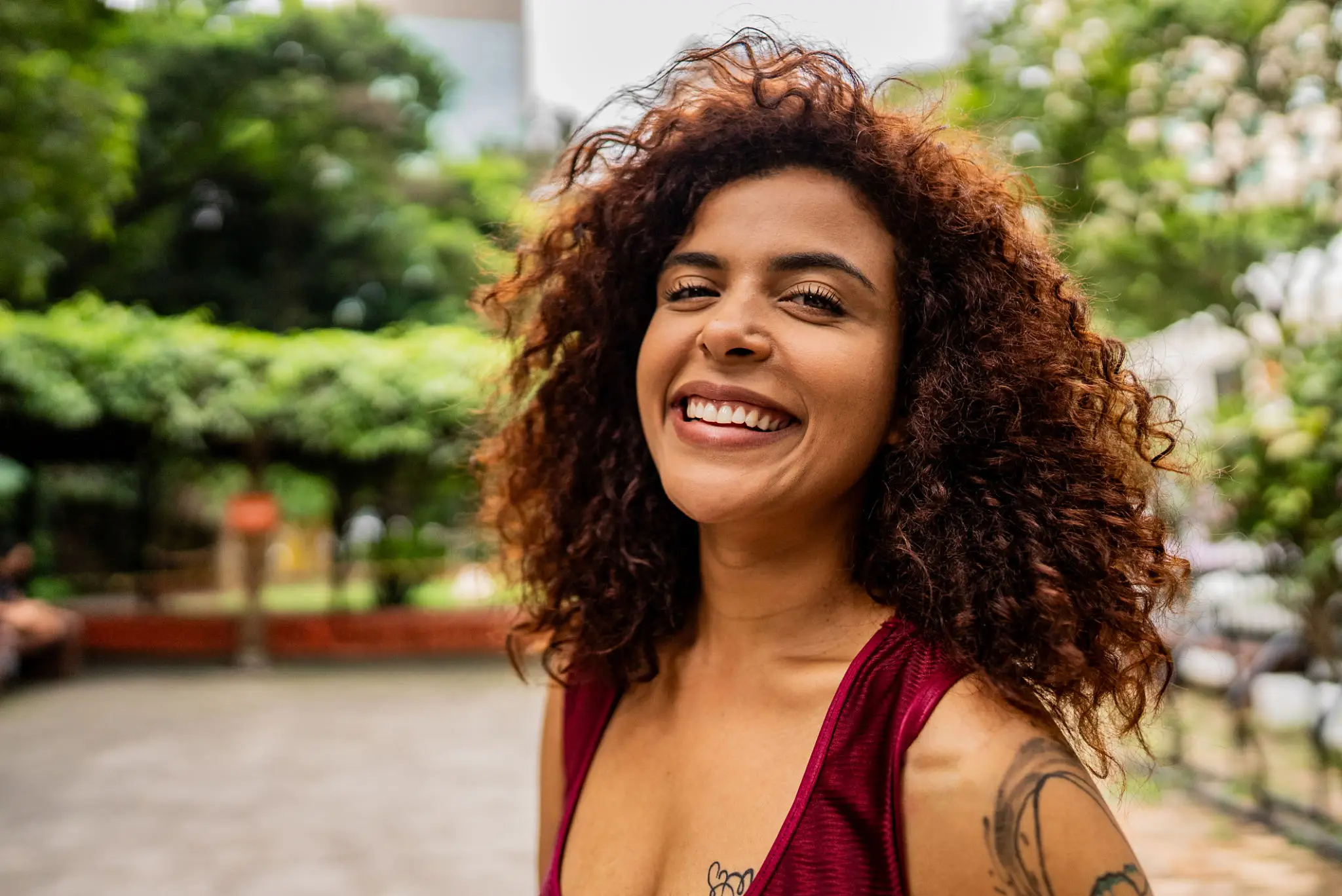 Smiling woman with curly hair outdoors in a casual setting.