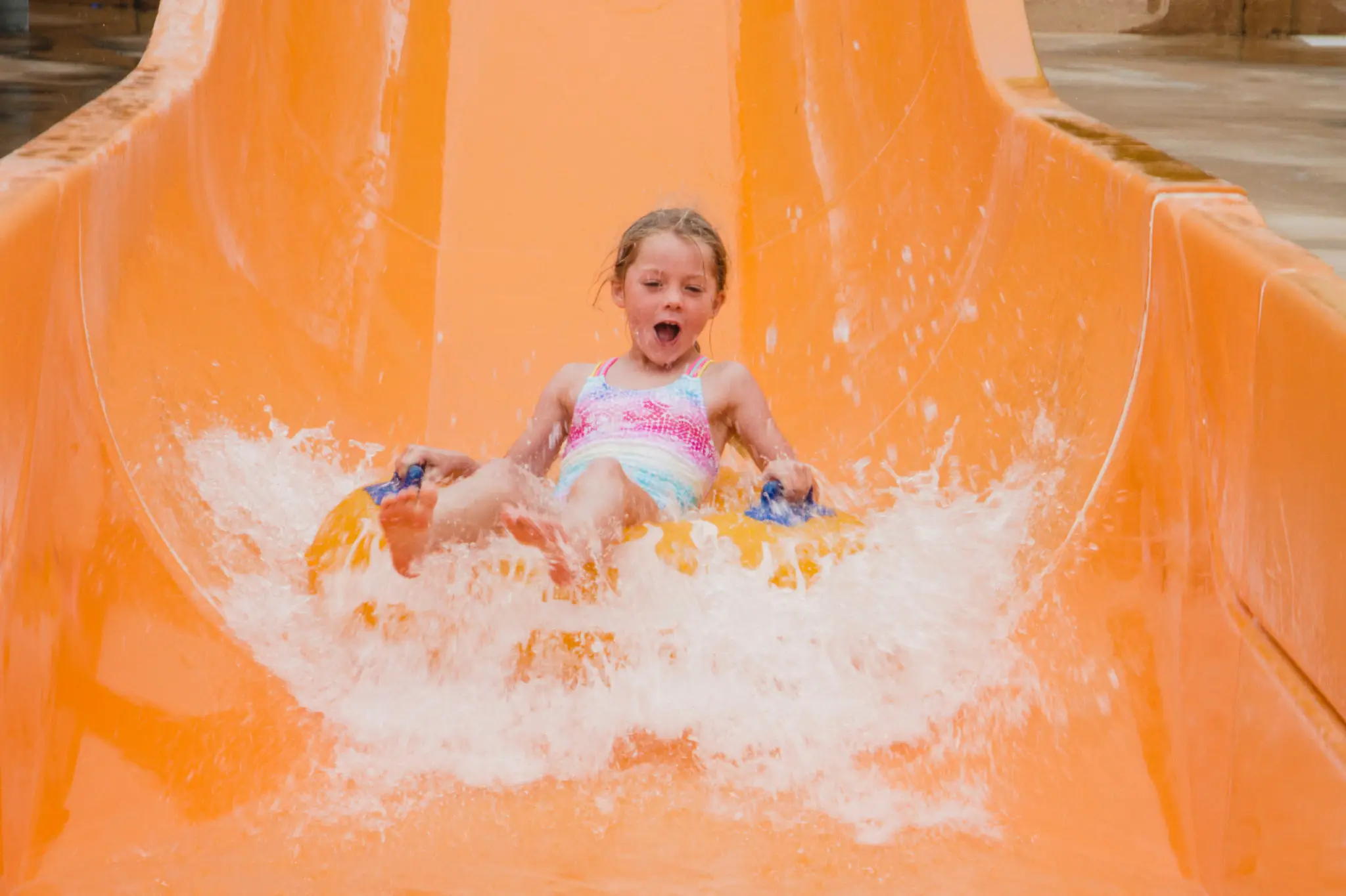 A joyful child splashing down an orange water slide.