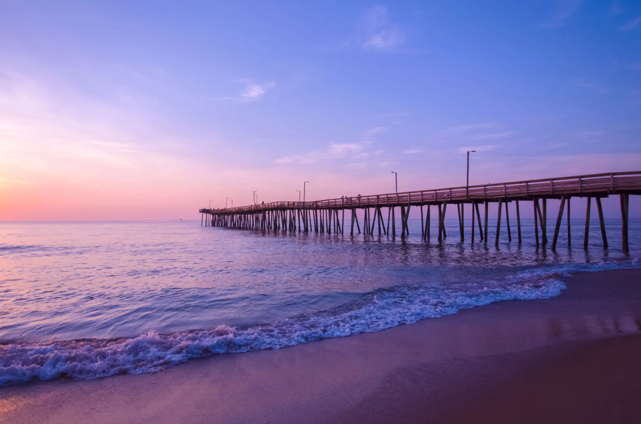 Sunset over a calm ocean with a long pier extending into the water.
