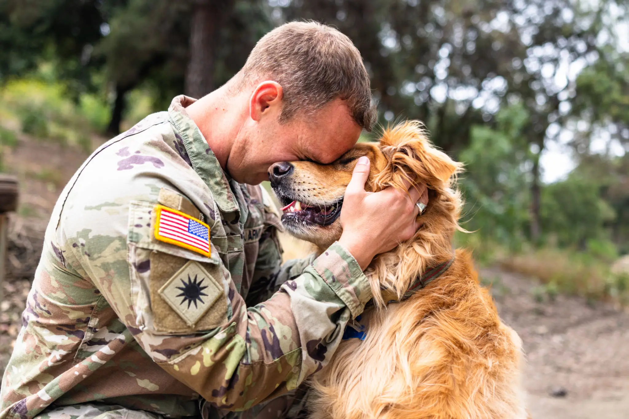 A soldier affectionately hugs a dog outdoors.