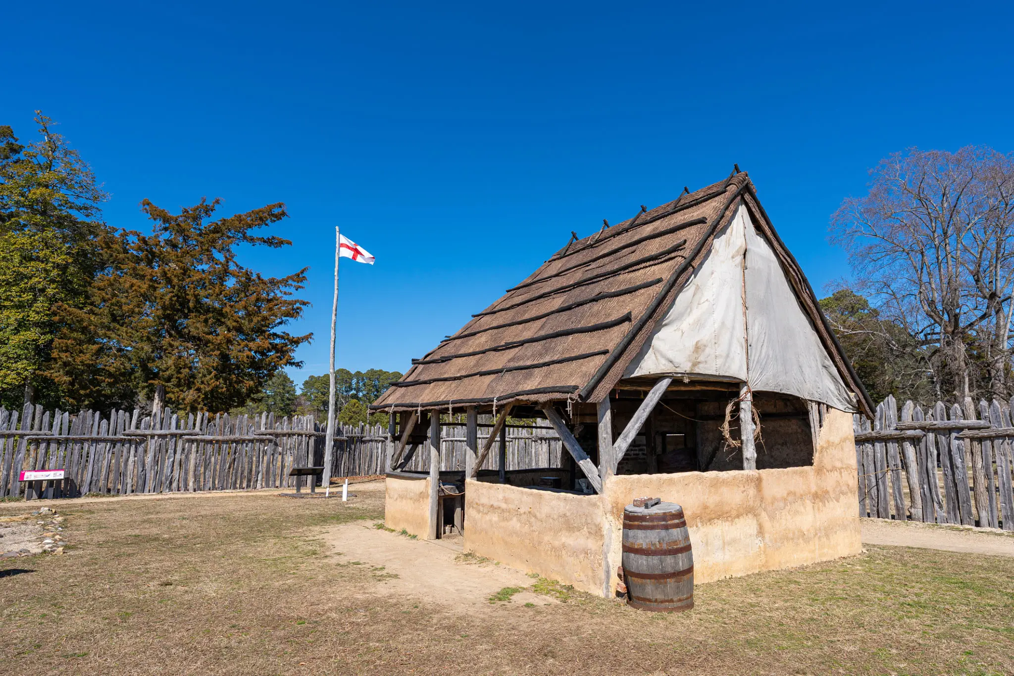 Reconstructed historic wooden building with a thatched roof under a clear blue sky.